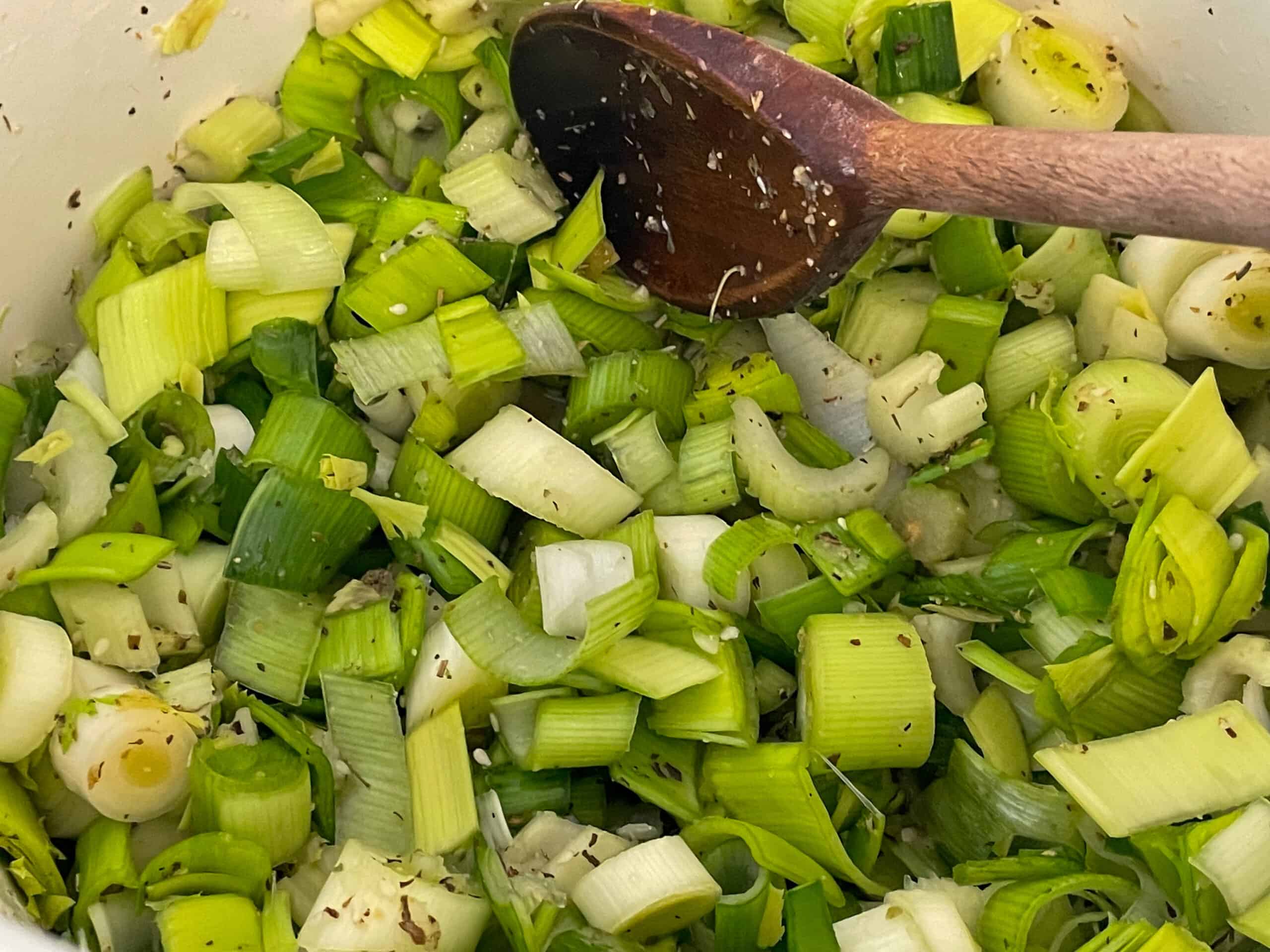 Sautéing leeks, celery, and garlic in veggie broth in a large soup pot with wooden spoon.