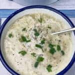 Chowder served in white bowl with blue rim and silver spoon, chopped chives scattered over.