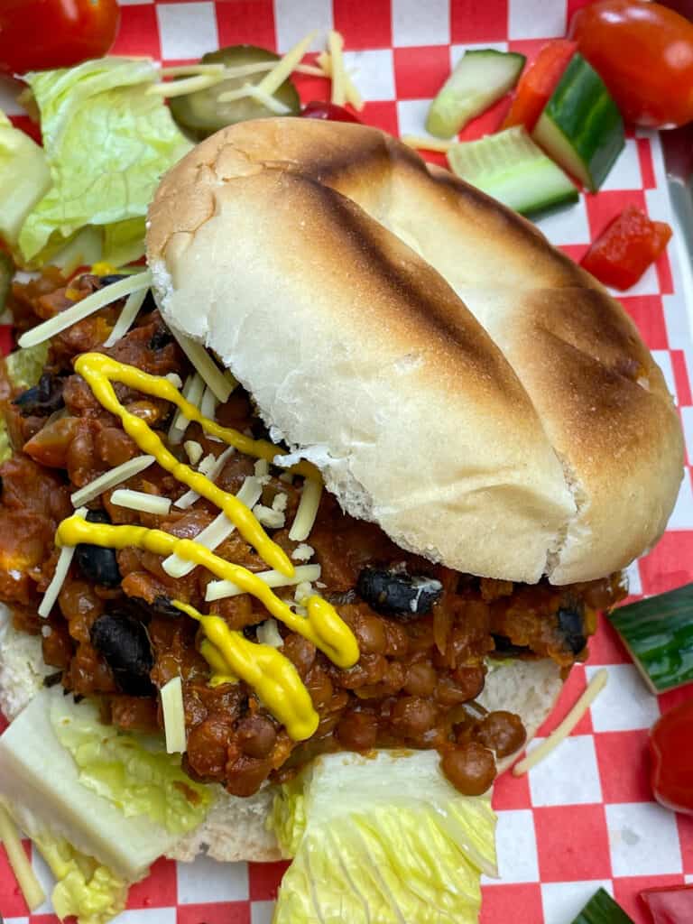 close up of sloppy joe on bread bun, with mustard streaks and vegan cheese.