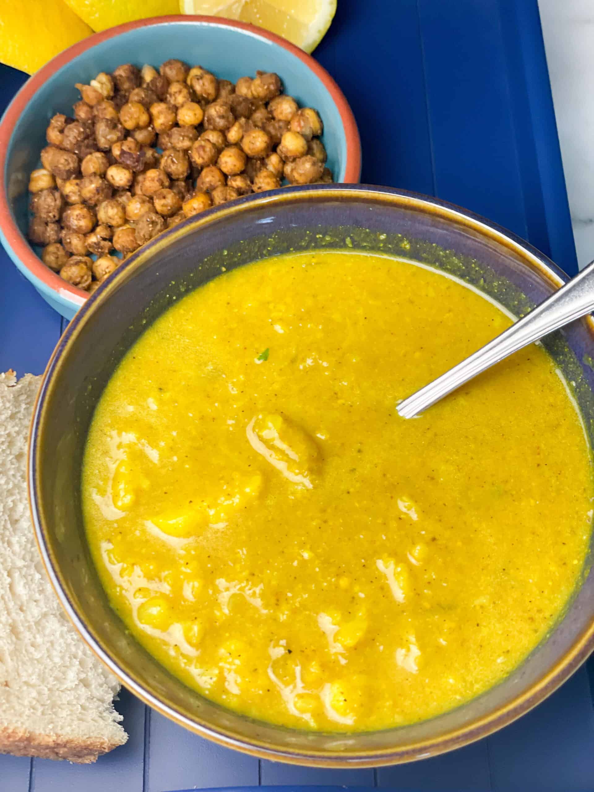 Cauliflower soup with chickpeas crouton dish to side, bread to side and silver spoon in the bowl.