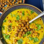 close up of curried cauliflower soup in blue bowl with gold rim, crispy chickpeas in small blue bowl to side.