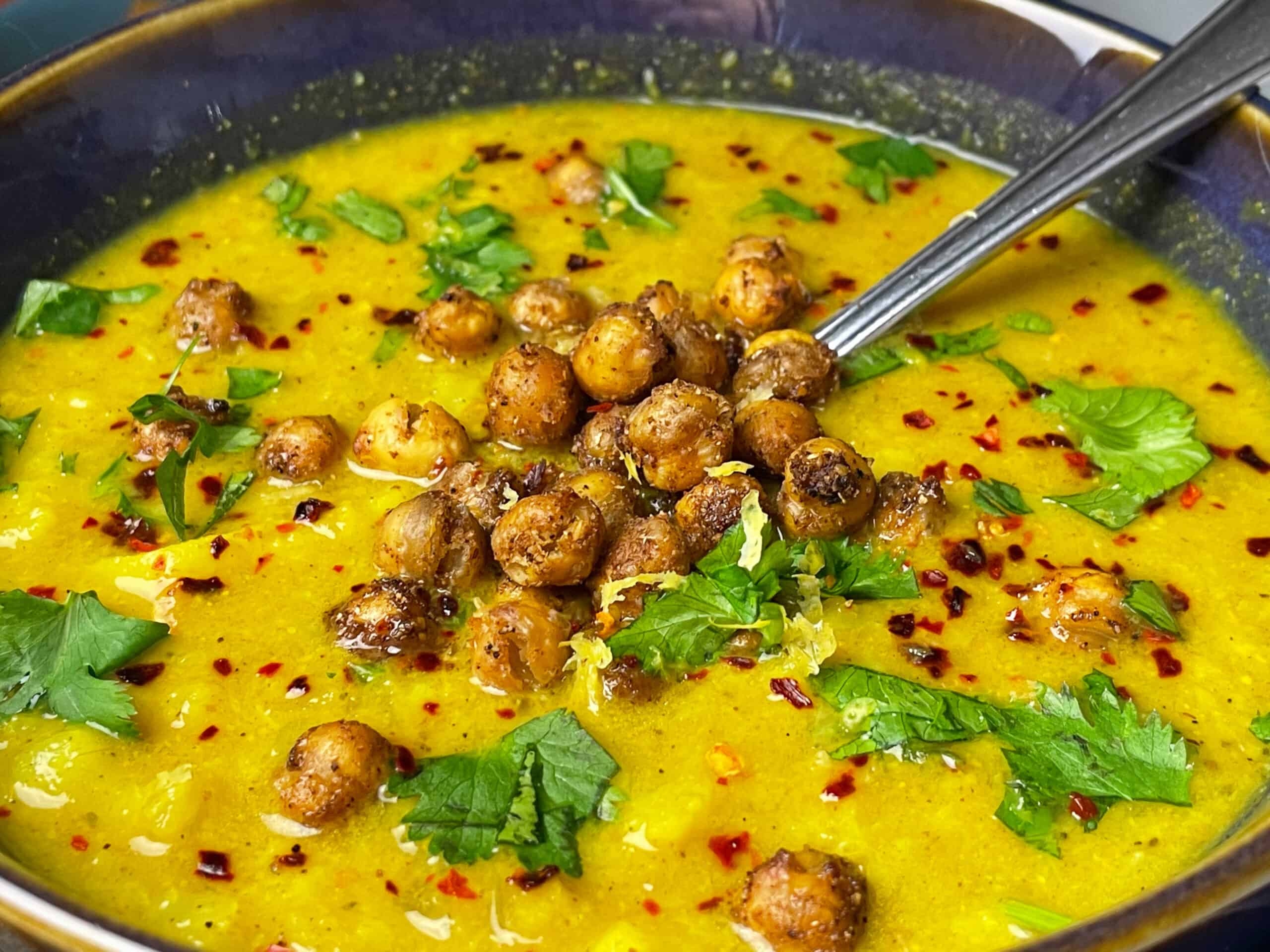 Close up of soup with chopped coriander, red pepper flakes and crispy chickpea croutons.