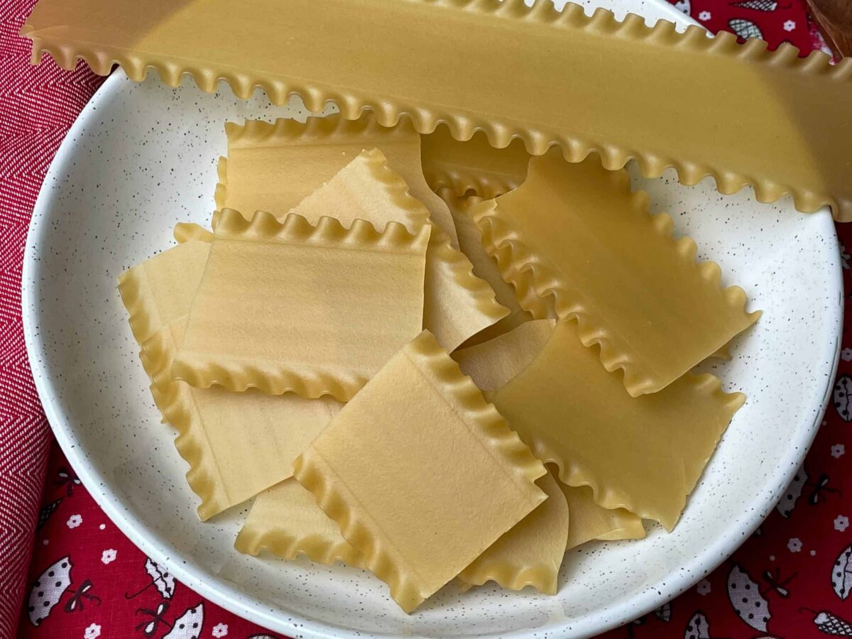 pieces of dried uncooked lasagne sheets in white bowl.