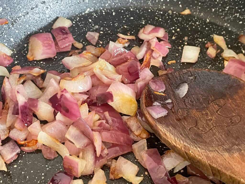 red onions and garlic cooking in black pan, with wooden spoon.