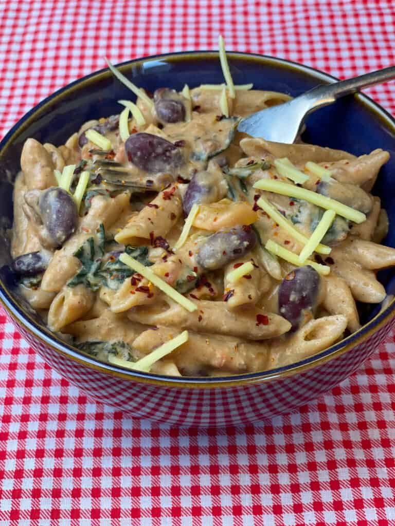 Blue bowl of chilli mac and cheese with fork and red check background.