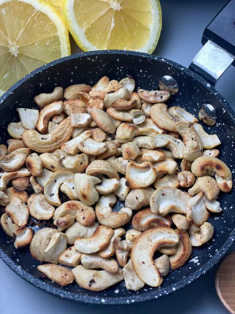 small granite fry pan with toasted cashews, lemon wedges to side.