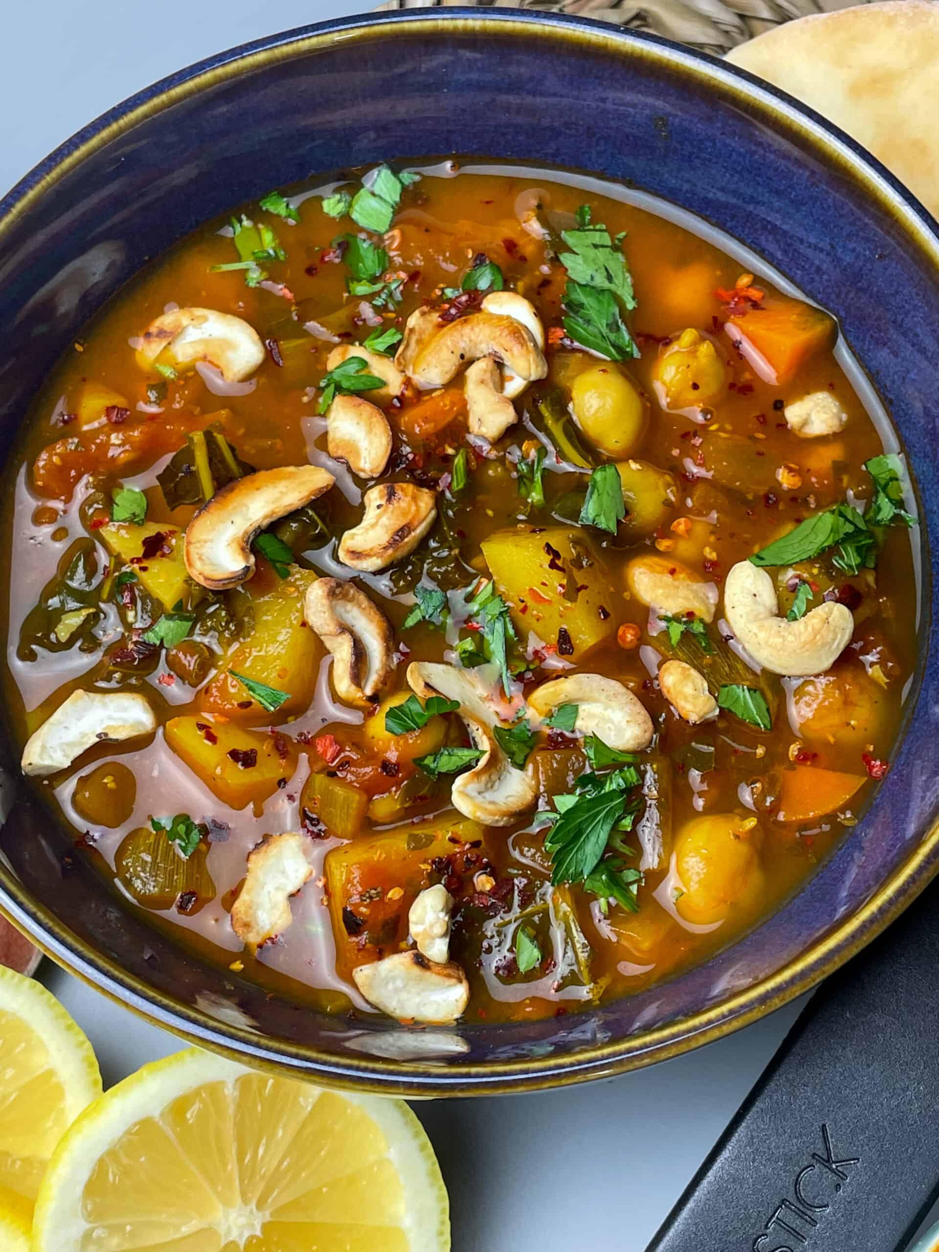 Blue bowl with gold rim full of spicy chickpea soup, lemon slices to side.