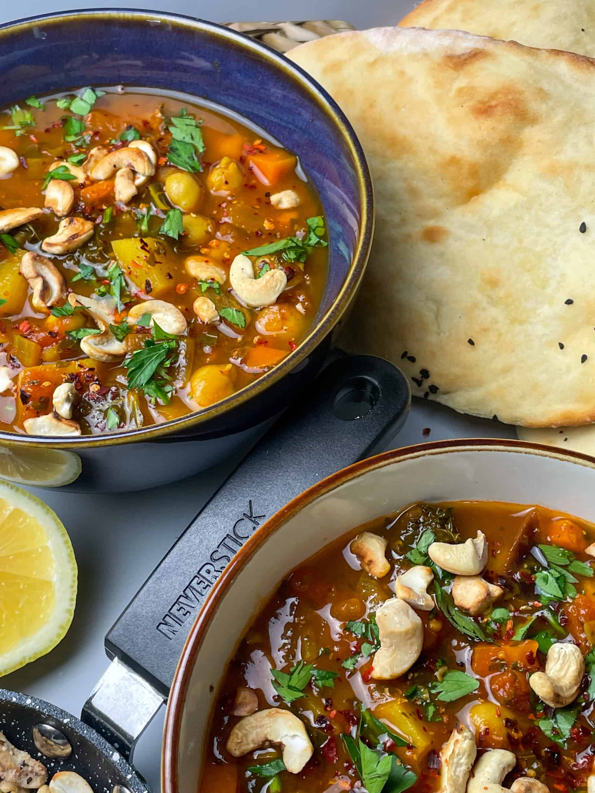 Two side views of bowls of chickpea soup, with naan breads to side, a small glimpse of fresh lemon and a skillet handle to side.
