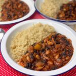 three bowls of black bean chilli with quinoa sitting on red check tea towel.