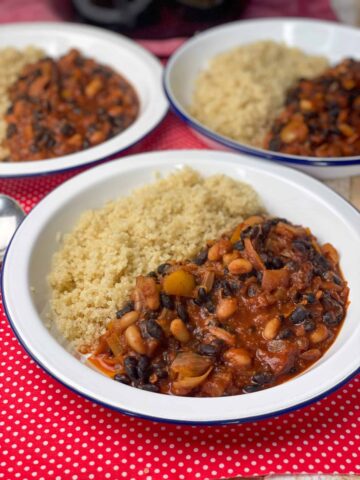 three bowls of black bean chilli with quinoa sitting on red check tea towel.
