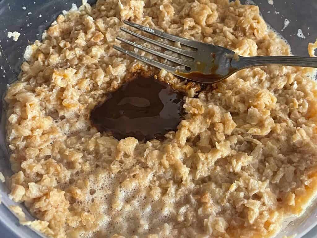 Textured vegetable protein soaking in water with a teaspoon of marmite, and silver fork at side.