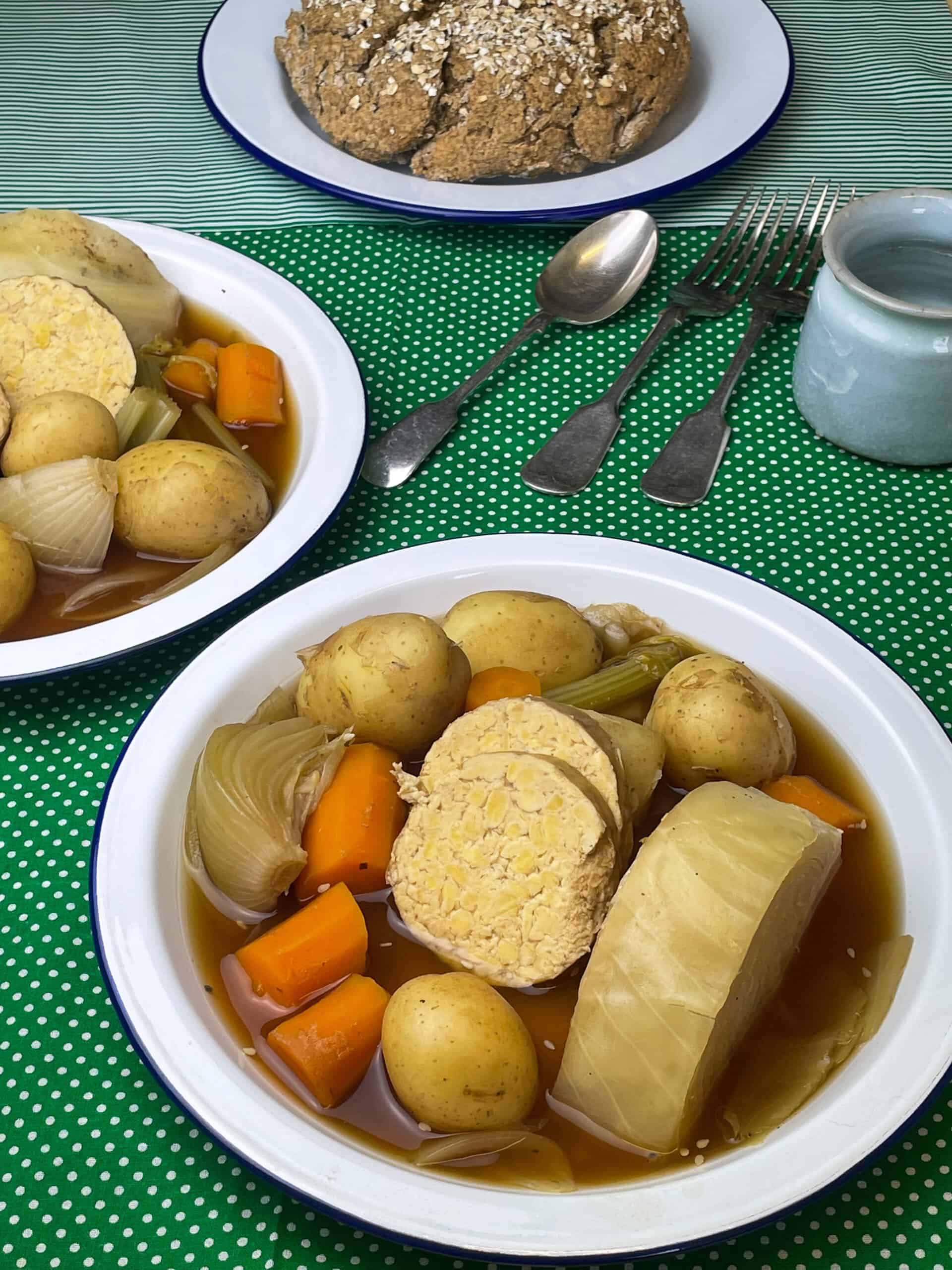 Two white enamel bowl with veggie stew, cutlery to side, green spotty background, small cup to side.