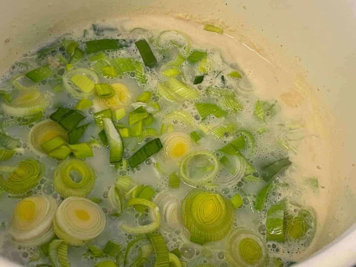 Leeks added to milky stock in soup pan.