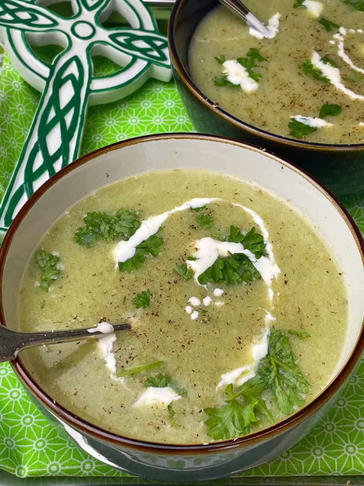 Close up bowl of broth with green Irish Celtic cross in background and green tablecloth with shamrock pattern.