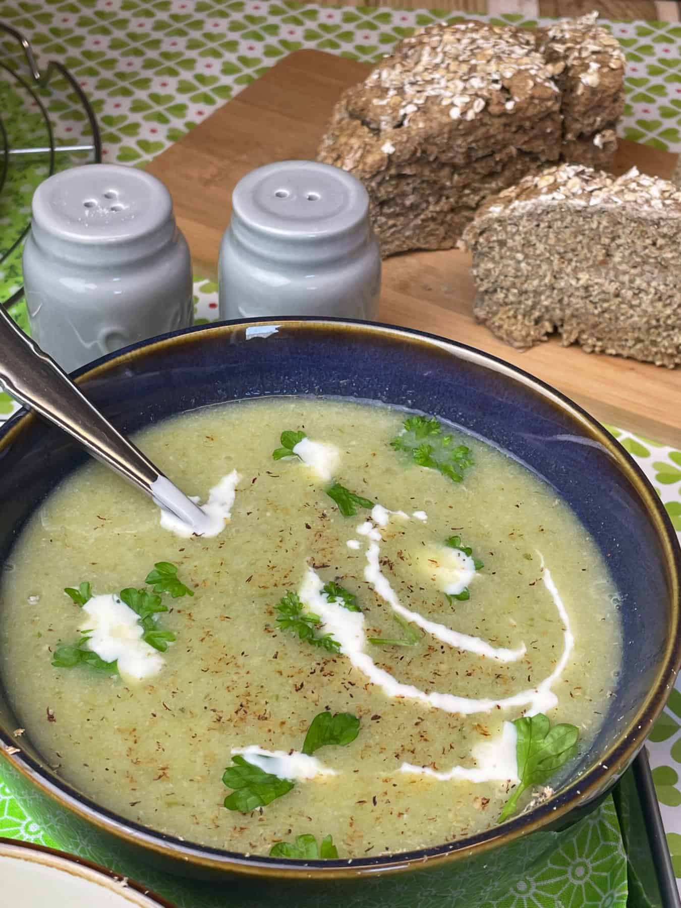 Irish leek and oatmeal broth served in blue bowl with parsley and cream garnish, soda bread to background.