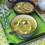 Two bowls of oatmeal leek broth on tray, with green flower tea towel, green and white celtic cross to side, white jug of cream to side, shamrock background,featured image.