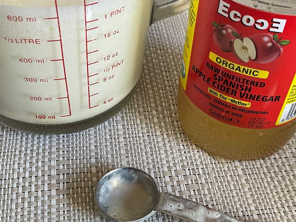 Apple cider vinegar, jug of plant milk and measuring spoon on cream mat.