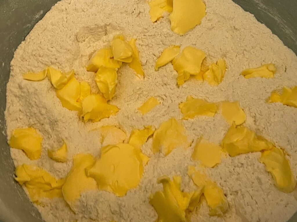 Margarine in little bits added to scone flour mix in bowl.