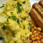 wartime champ with chopped parsley, baked beans and sausages at the side of the white plate.