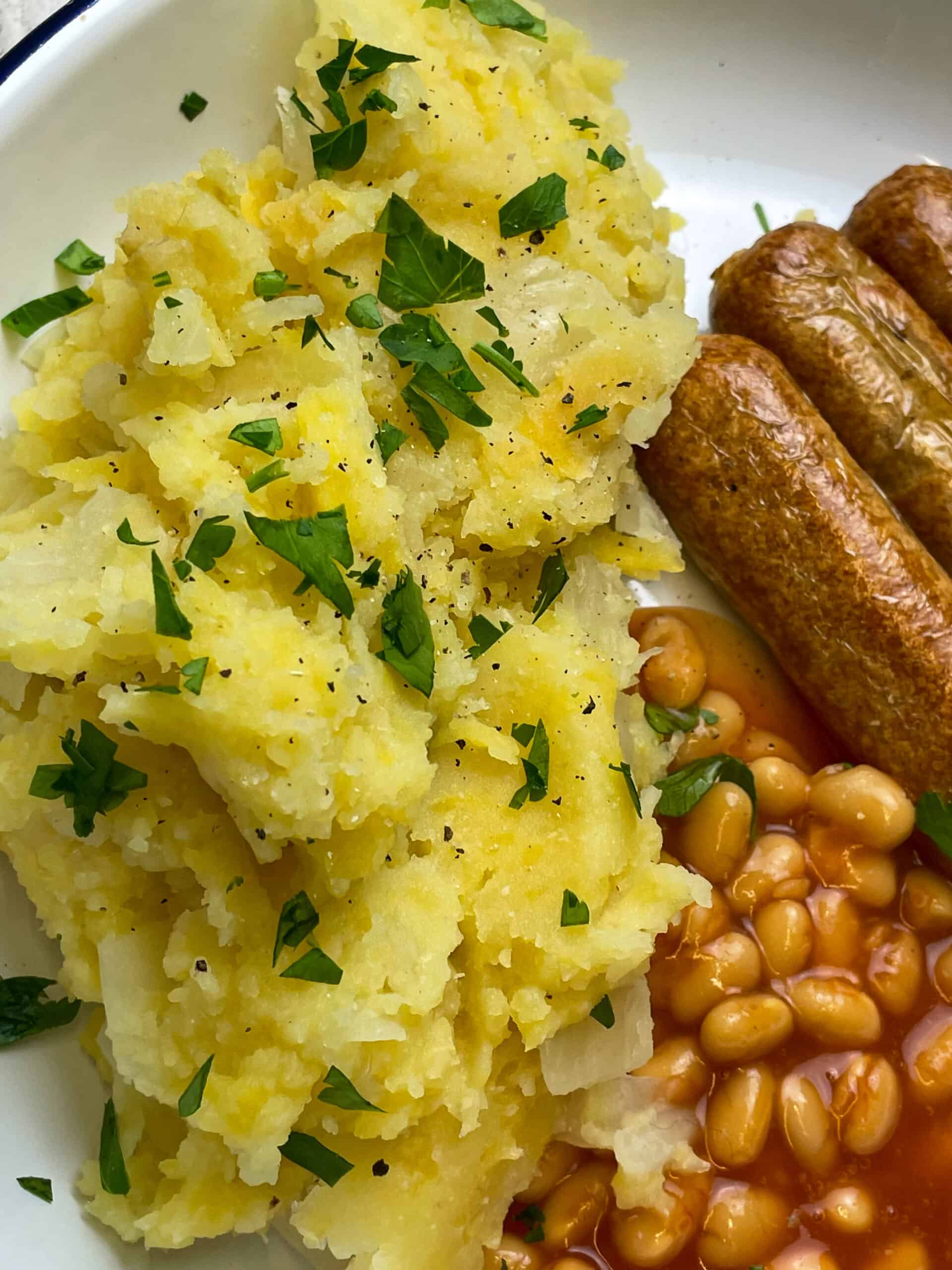 wartime champ with chopped parsley, baked beans and sausages at the side of the white plate.