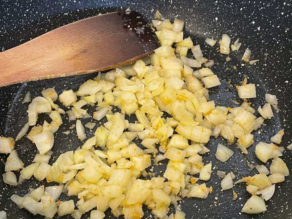 onions and garlic cooking in black granite pan with wooden spatula.