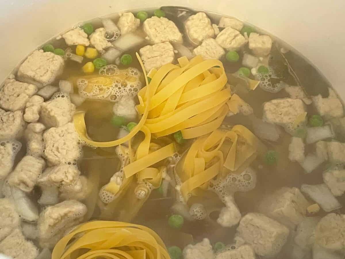 Pasta noodles added to soup in pot.