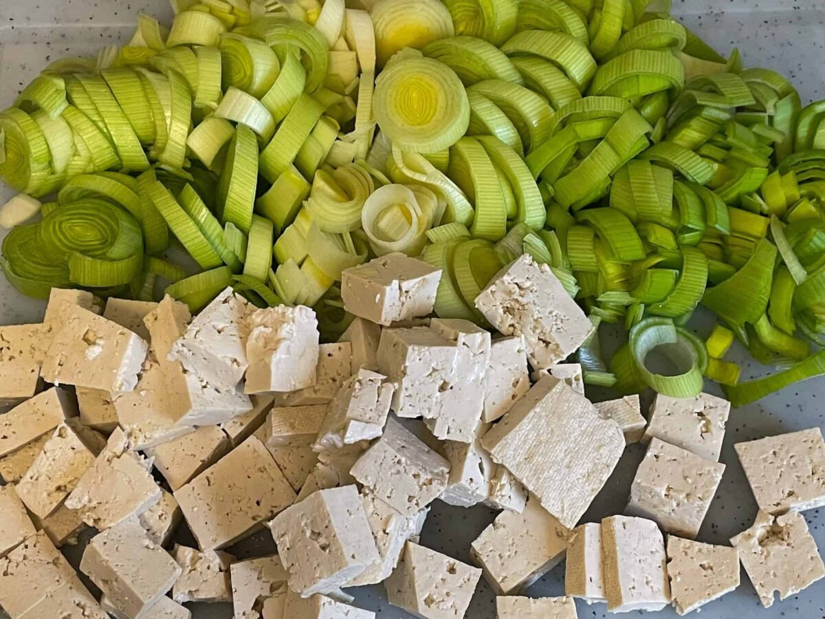 Sliced leeks and chopped tofu on chopping board.