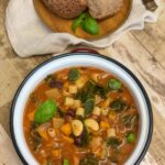 Bowl of Minestrone soup with brown wood plate with crusty bread, light brown wood background.