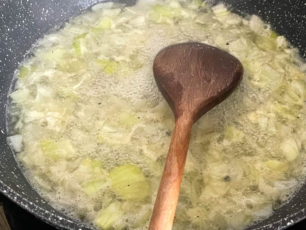 onions and garlic sautéing in skillet with wooden spoon.