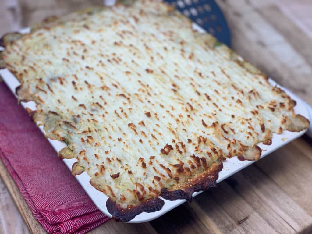 Vegan vegetable hotpot baked golden and crispy, sitting on red tea towel on wooden board.