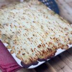 Vegan vegetable hotpot baked golden and crispy, sitting on red tea towel on wooden board.