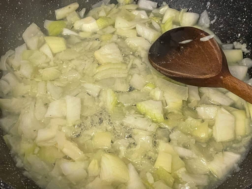 Onions cooking in veggie stock in skillet, with wooden spoon.