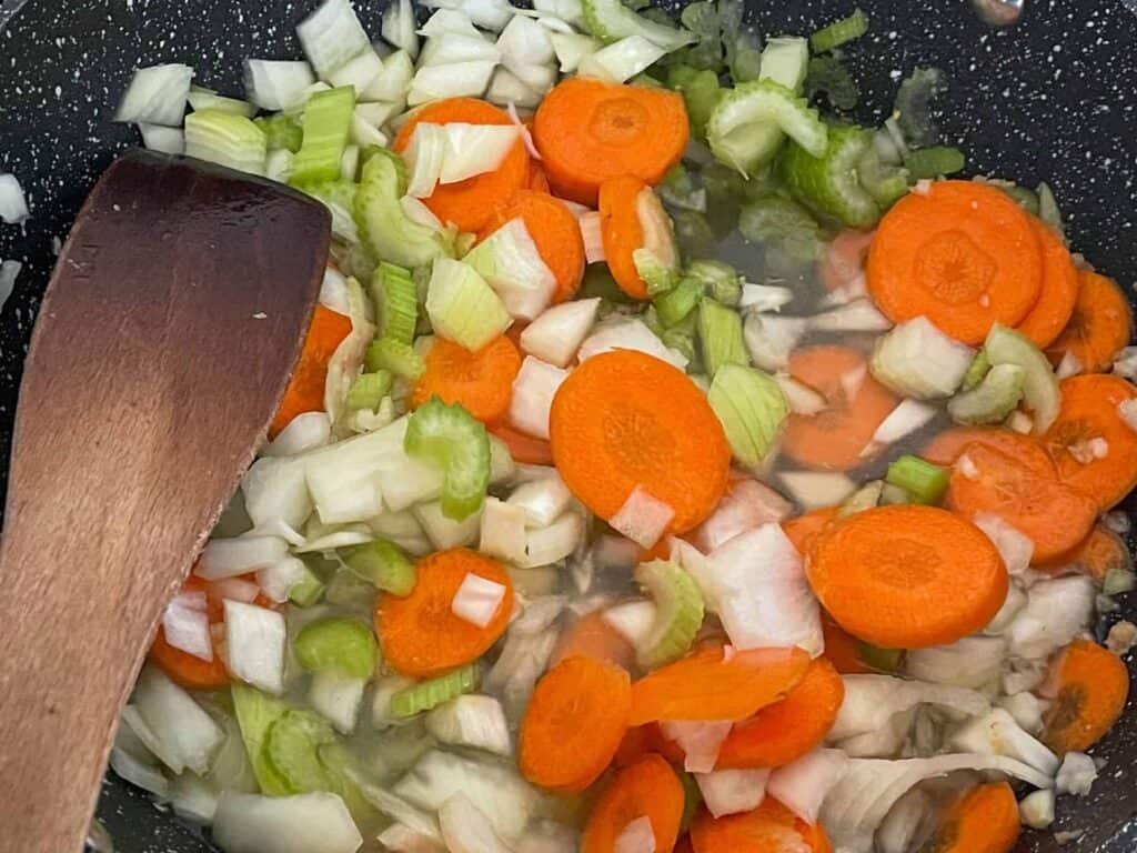 carrot, celery and garlic cooking in skillet with wooden spatula.