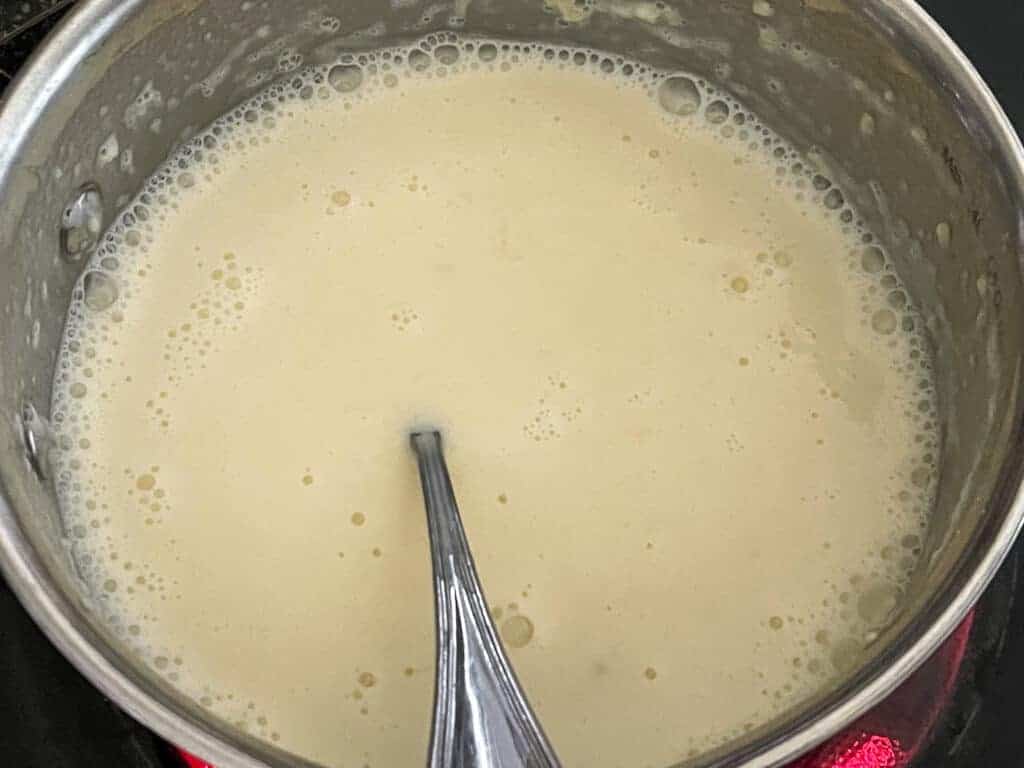 vegan cheese sauce being prepared in small silver pan with silver spoon.