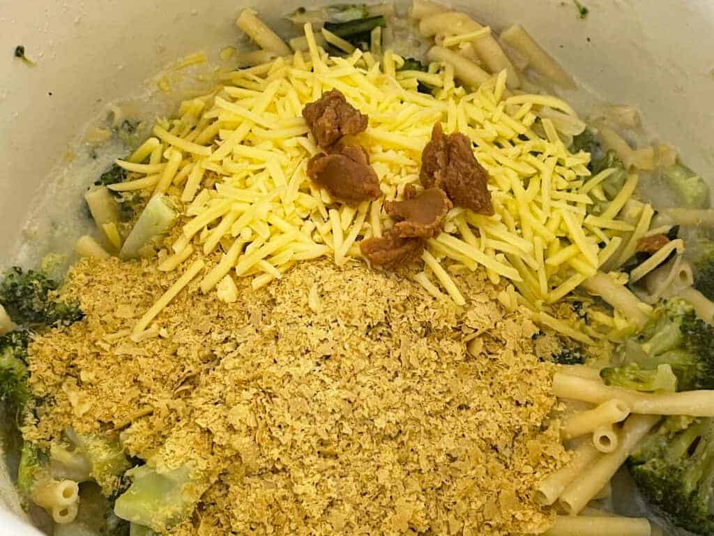 Yeast flakes, cheese, and miso paste added to cheesy pasta cooking in pot.