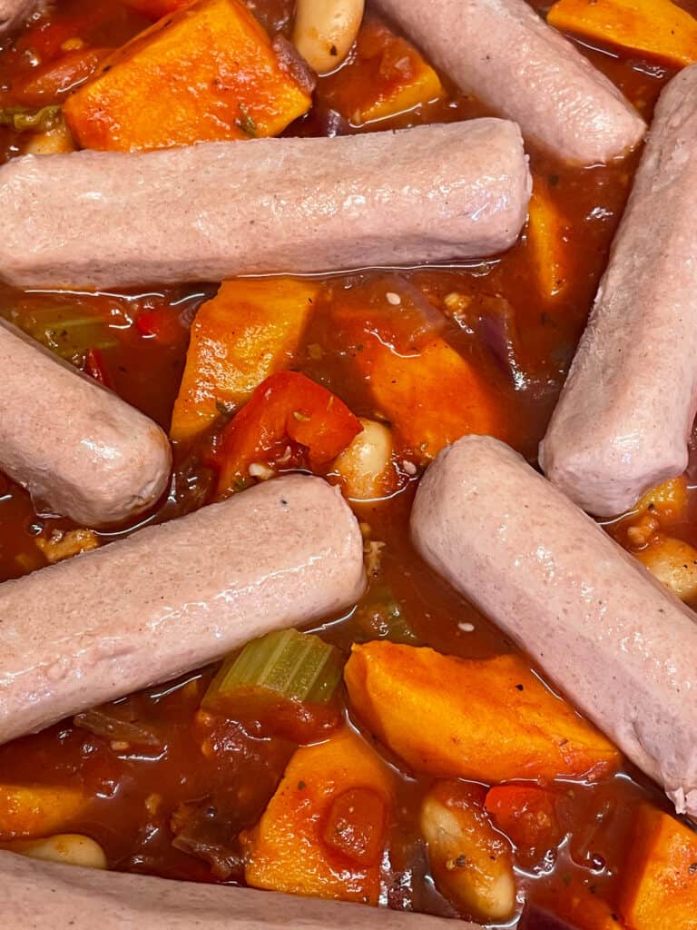 Uncooked meat-free sausages placed on top of veggie and tomato mix.