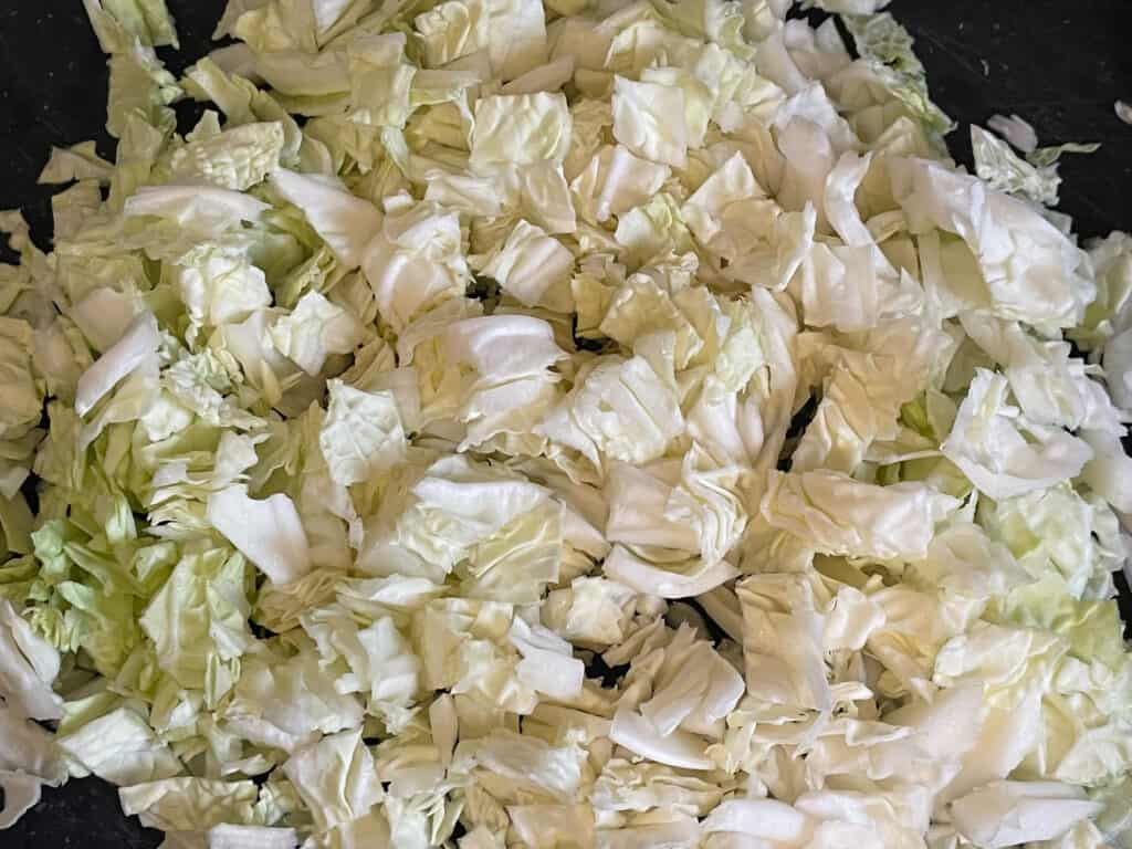 Chopped cabbage on black chopping board.