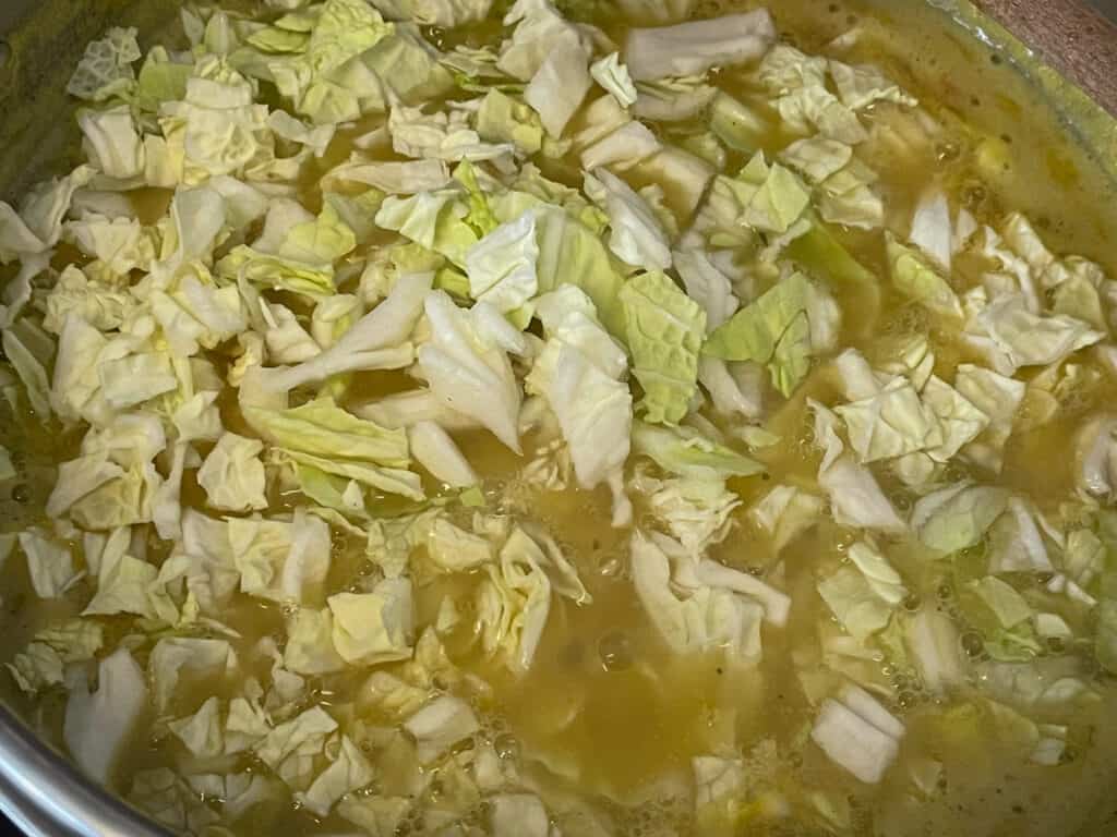 Cabbage mixed through broth in soup pan.