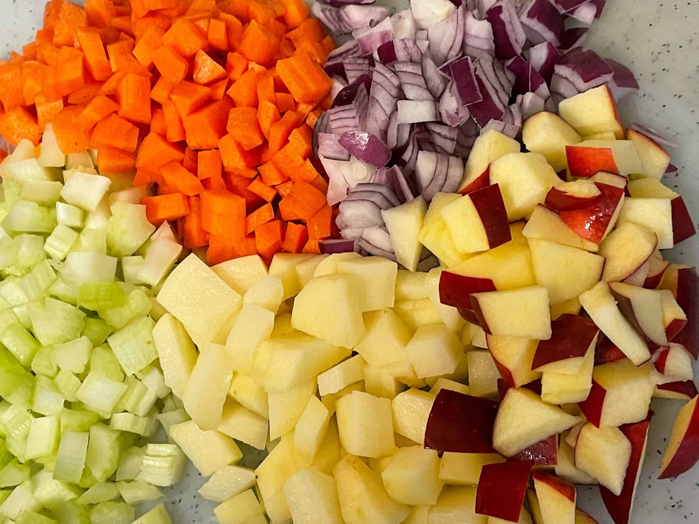 Soup veggies diced on a white chopping board.