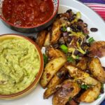 Loaded black bean potato wedges served with salsa and guacamole, with stripy background.