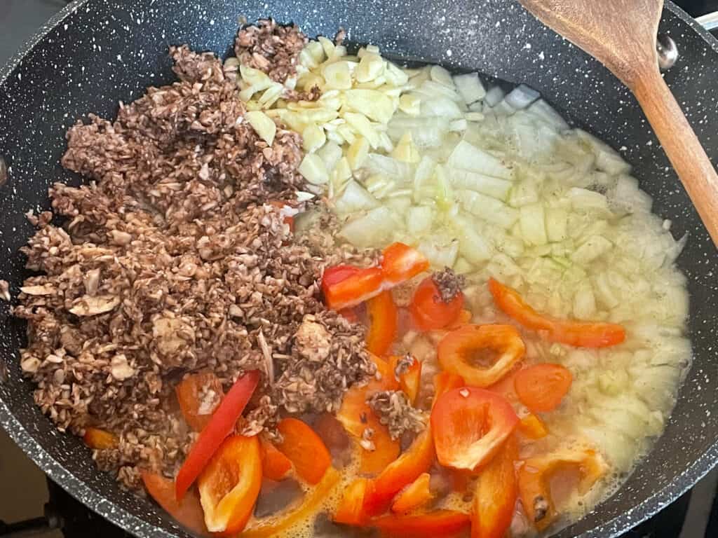 meat-free sausage pasta sauce ingredients in skillet with wooden spoon to side.