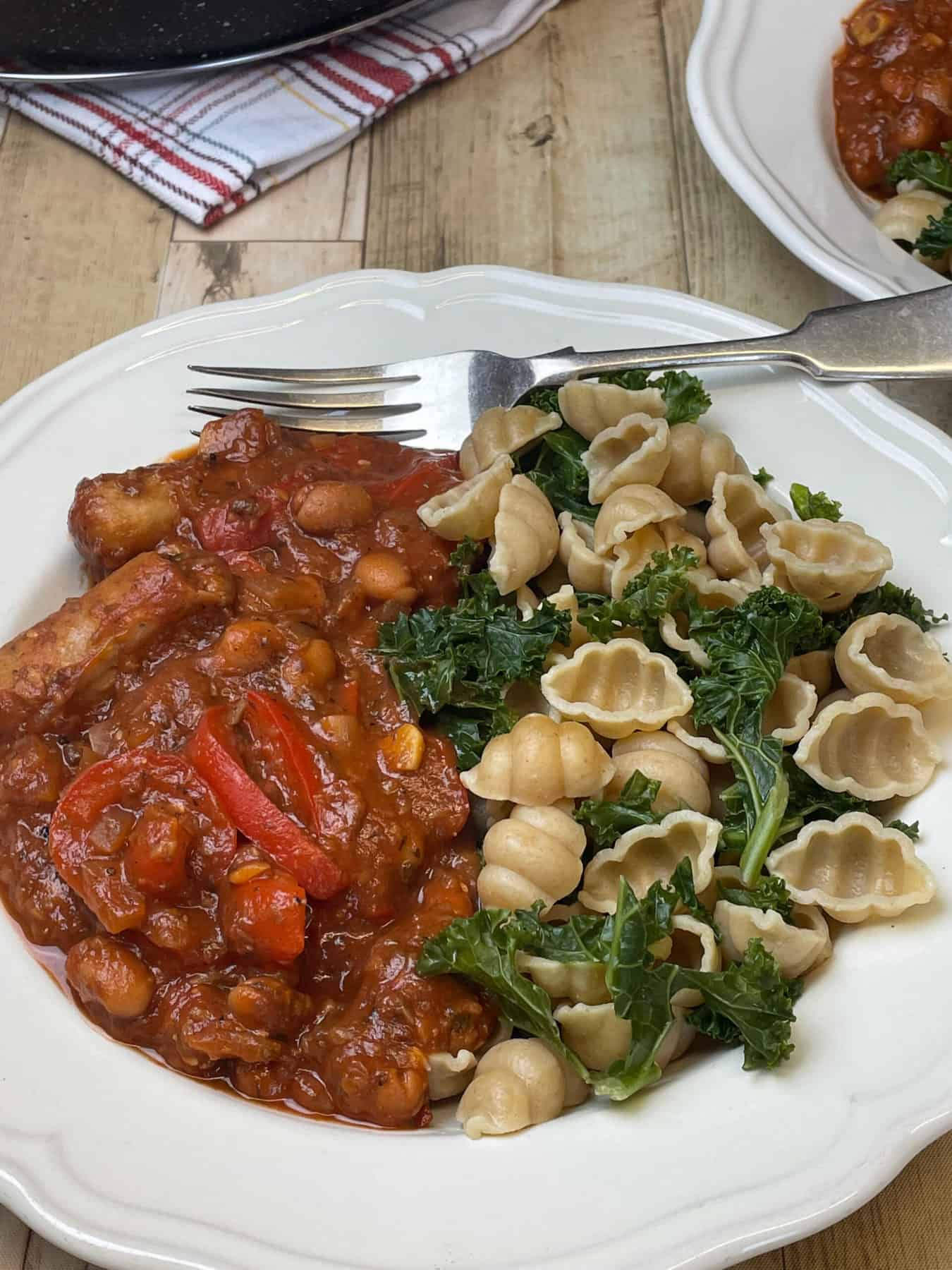 Bowl of vegan sausage pasta served with pasta shells and kale, silver fork and wood table background.