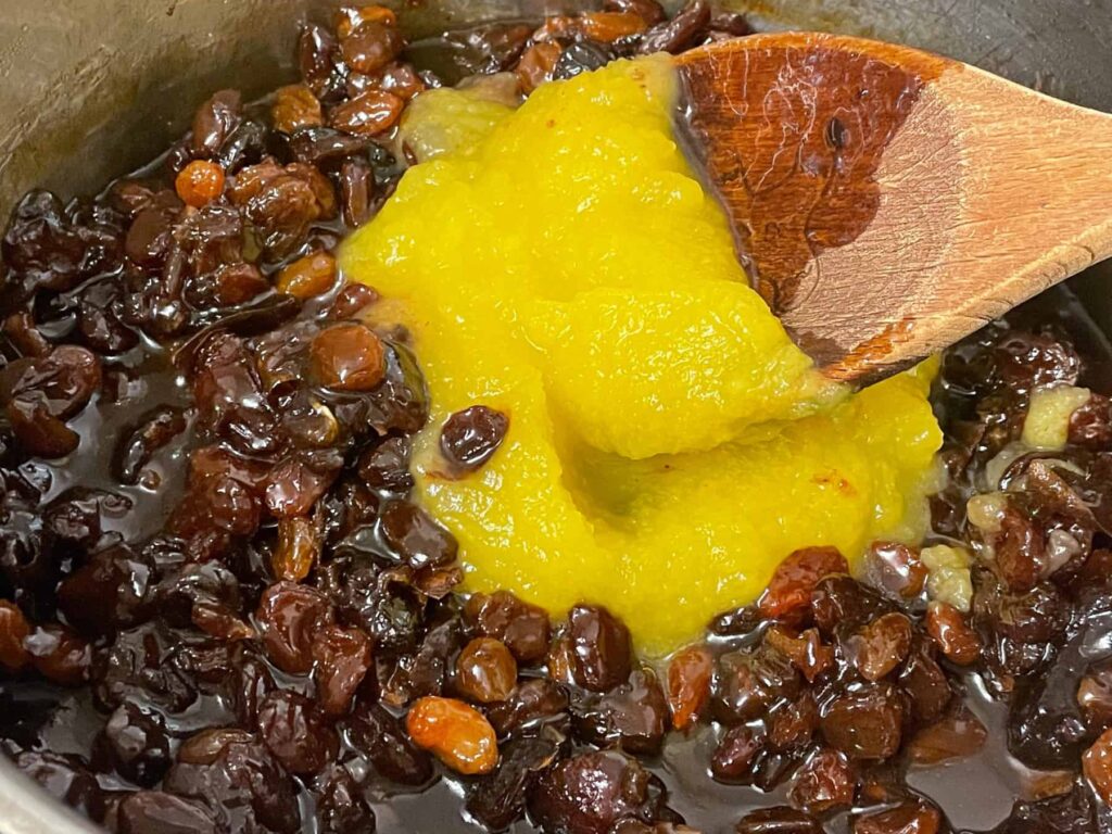 Pumpkin puree added to stewed dried fruit in saucepan with wooden spoon.