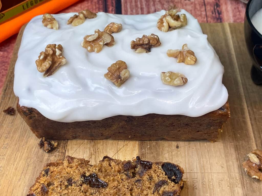 vegan pumpkin spiced fruit loaf cake with cream cheese frosting and chopped walnuts, wooden chopping board.
