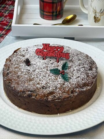 Christmas cake served on white cake plate with tea tray to side.