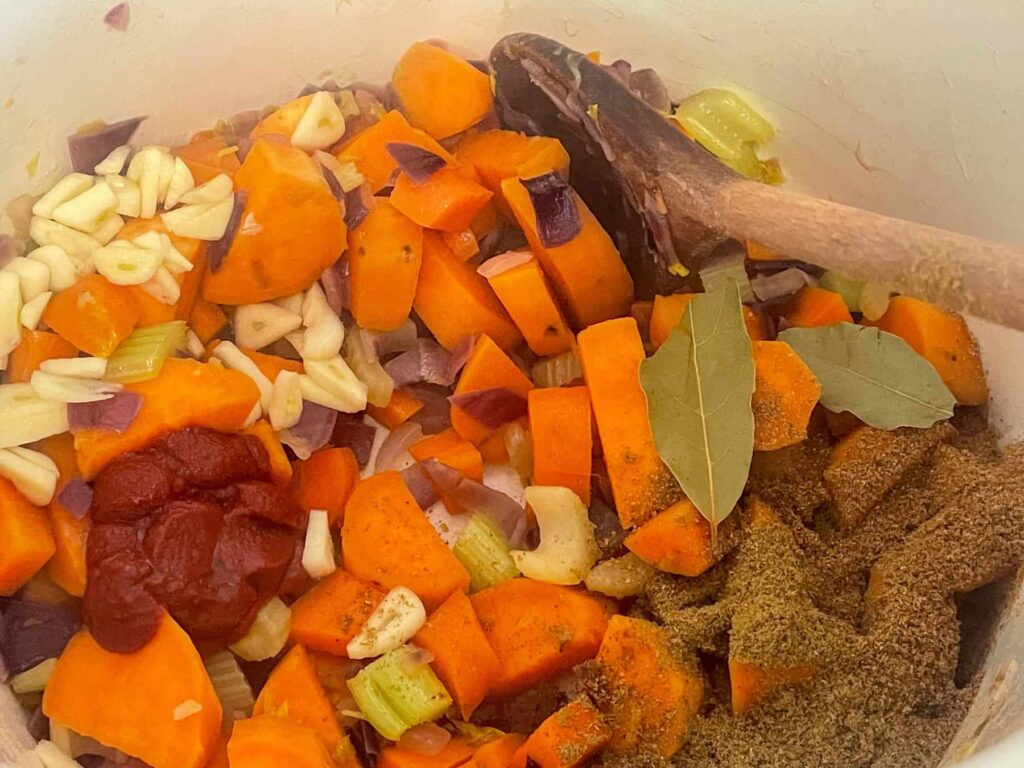 Vegan butternut squash lasagna veggies cooking in pan with wooden spoon.