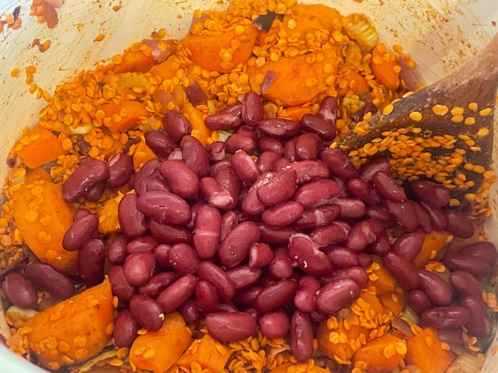 Kidney beans and lentils added to veggies in pan.