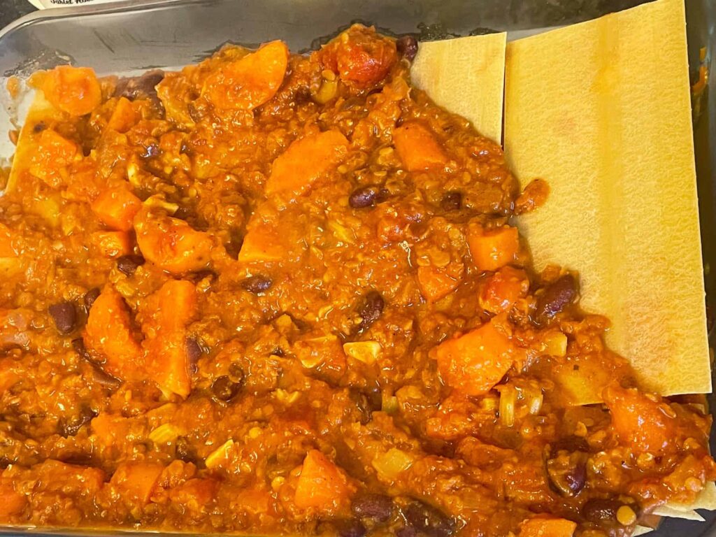 Lentil lasagna being layered with pasta sheets and sauce in baking dish.