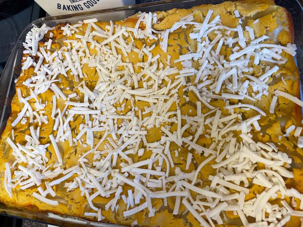 Grated vegan cheese sprinkled over baked lentil lasagna ready to go back in the oven to melt.