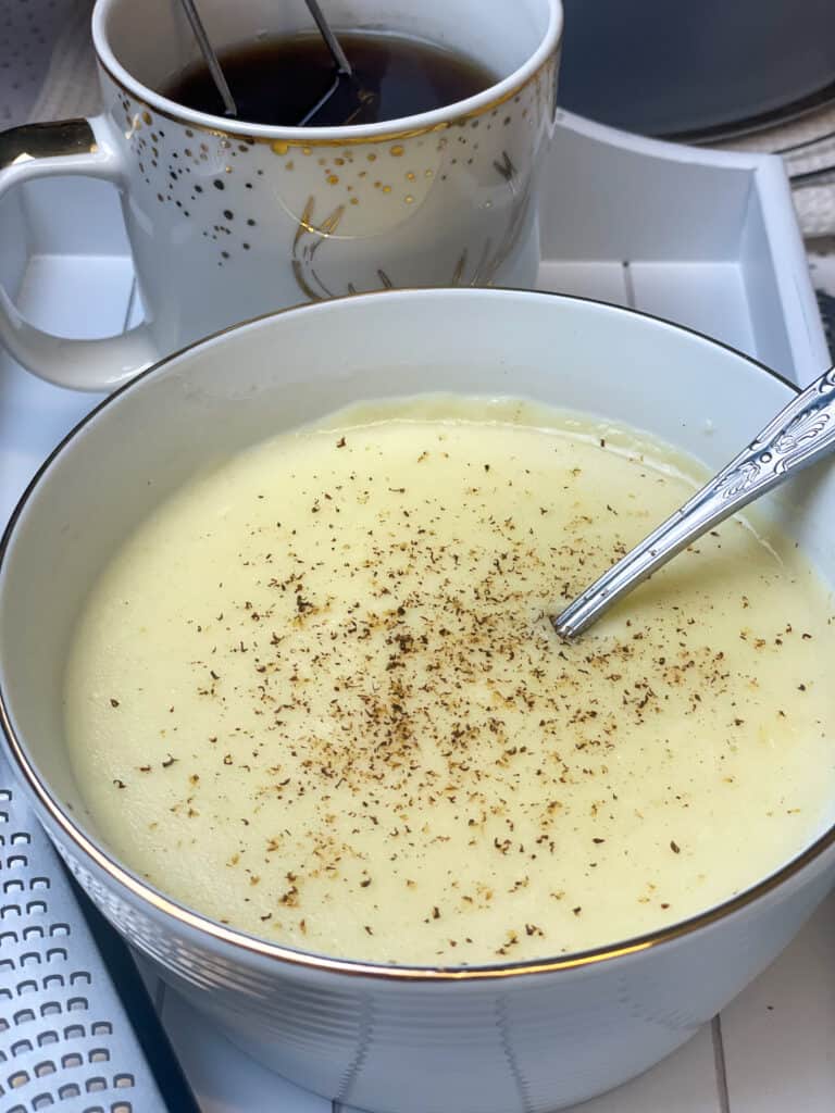 close up of vegan British semolina pudding in bowl with mug of herbal tea to side.